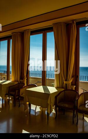 I tavoli di un hotel con una splendida vista sul mare dalla finestra. La luce entra attraverso la finestra in una giornata estiva. Vacanze, relax, lusso, Foto Stock