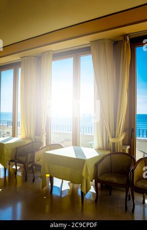 I tavoli di un hotel con una splendida vista sul mare dalla finestra. La luce entra attraverso la finestra in una giornata estiva. Vacanze, relax, lusso, Foto Stock