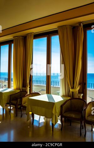 I tavoli di un hotel con una splendida vista sul mare dalla finestra. La luce entra attraverso la finestra in una giornata estiva. Vacanze, relax, lusso, Foto Stock