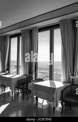 I tavoli di un hotel con una splendida vista sul mare dalla finestra. La luce entra attraverso la finestra in una giornata estiva. Vacanze, relax, lusso, Foto Stock