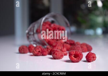 vetro trasparente con lamponi su tavolo bianco in cucina grigia. Foto di alta qualità Foto Stock