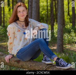 Bella adolescente o giovane femmina adulto con capelli rosso scuro, pelle fiera, e gli occhi verdi blu che posano in abiti casual su accesso Estate Pennsylvania Woods Foto Stock