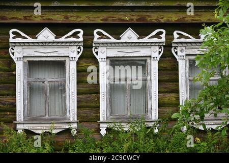 Listelli scolpiti sulle finestre delle case di legno russe. La scultura adorna la vecchia finestra. Le pareti della casa dai vecchi tronchi da vicino. Antico tipico Foto Stock