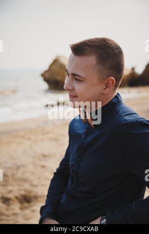 Cerimonia nuziale sulla spiaggia all'aperto vicino all'oceano, elegante e felice sposo sorridente in camicia blu scuro con cravatta di legno Foto Stock