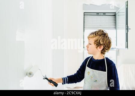 Ragazzo aiuta la sua famiglia a dipingere un muro bianco. Foto Stock