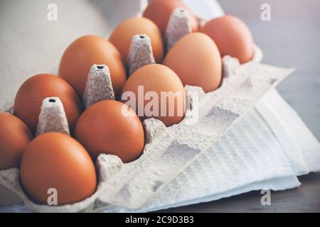 Sul tavolo da cucina grigio è un asciugamano bianco e un negozio - acquistato scatola di cartone contenente un uova di pollo marrone. Prodotti di origine animale. Foto Stock