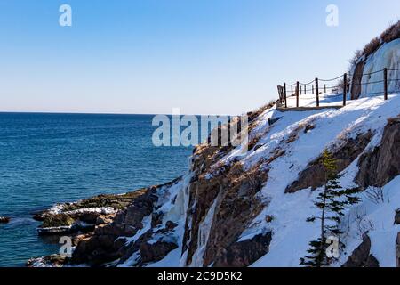 Un sentiero curvo lungo il fianco di una montagna rocciosa con un binario di sicurezza. È inverno e c'è neve bianca a terra. Foto Stock