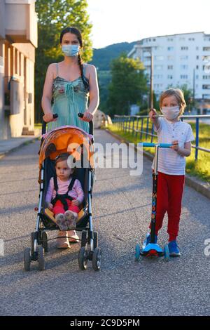 Bambini con madre che camminano per strada con maschere per COVID-19. Isolamento di sé e distanziamento sociale. Foto Stock