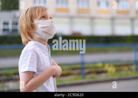 Piccolo ragazzo carino con maschera protettiva che guida uno scooter in un parco. Foto Stock
