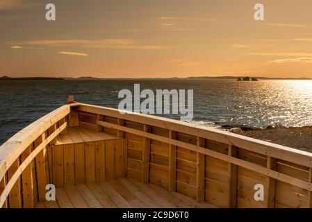 Arco di legno di una barca da pesca con l'oceano sullo sfondo. L'orizzonte del mare è arancione luminoso con un po' di cielo blu, sporadiche nuvole e piccole isole. Foto Stock