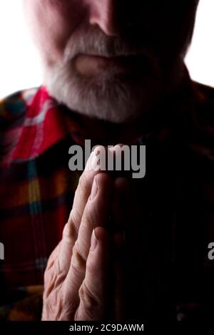 Un uomo con una barba all'età tiene insieme le mani, una preghiera e una richiesta - silhouette, isolare Foto Stock