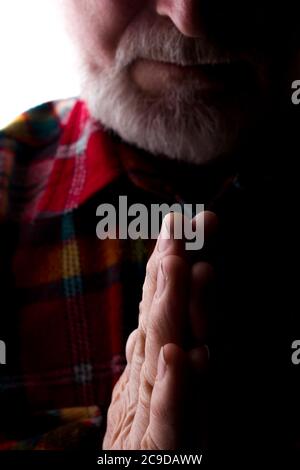 Un uomo con una barba all'età tiene insieme le mani, una preghiera e una richiesta - silhouette, isolare Foto Stock