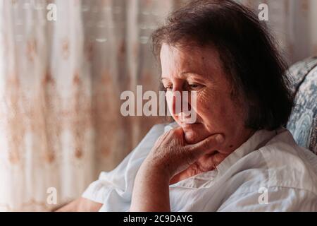 Primo piano ritratto di una donna anziana seduta sulla sedia, mano sulla testa, guardando preoccupato Foto Stock