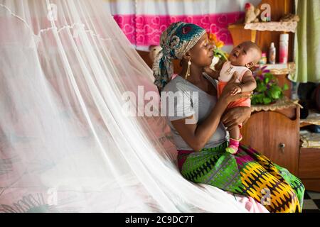 Una giovane madre africana e la sua bambina dormono sotto una zanzariera di notte per tenerle al sicuro dalla malaria a Kouroussa, Guinea, Africa occidentale. Foto Stock