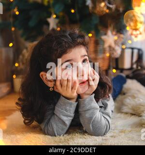 Ritratto di Natale di bella bambina sdraiata sul pavimento sotto l'albero di natale. Vacanza invernale Natale e Capodanno concetto Foto Stock