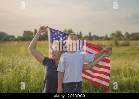 Il ragazzino lascia la bandiera americana volare in mano sul vento al campo verde. La famiglia patriottica celebra il giorno dell'indipendenza degli stati uniti il 4 luglio. Co Foto Stock