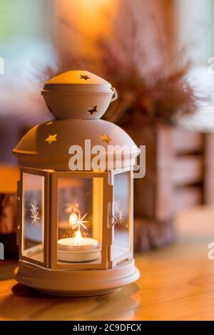 Bella lanterna bianca con candela bruciante all'interno su tavolo di legno. Immagine tonata. Romantica lanterna bianca. Decorazioni natalizie Foto Stock