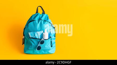 Concetto di ritorno a scuola durante la pandemia di Corona. Borsa con maschere mediche, disinfettanti e matite isolate su sfondo giallo. Nuove regole scolastiche Foto Stock