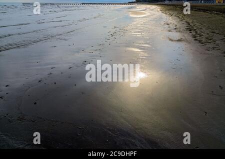 Spiaggia di sabbia bagnata e lucida alla luce del sole che affonda a grado, Italia Foto Stock