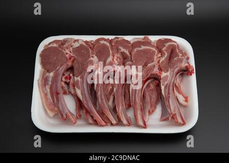 Costolette grezze di agnello (tagliole) in un contenitore bianco in polistirolo isolato su sfondo nero con spazio per la copia del testo Foto Stock