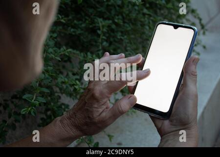 Una persona anziana che tocca il suo smartphone mentre tiene con una mano Foto Stock