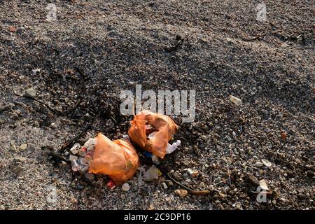 I sacchi di raccolta di colore arancione con i rifiuti sparsi su una spiaggia pubblica. Concetto di inquinamento oceanico. Foto Stock