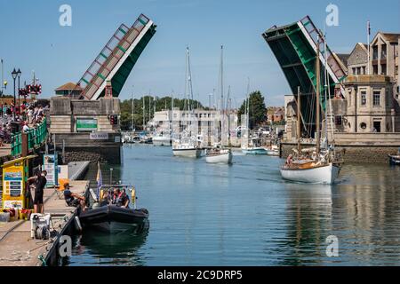 Tre yacht che navigano sotto il ponte di Weymouth con il ponte completamente aperto a Weymouth Harbour, Dorset, Regno Unito, il 22 luglio 2020 Foto Stock