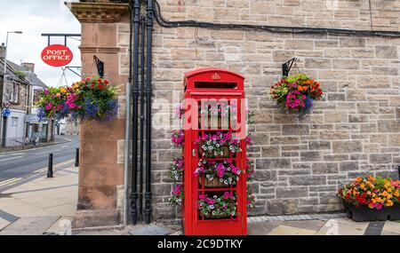 Iconico telefono rosso britannico convertito in cestini di fiori e segno dell'Ufficio postale, Tranent, East Lothian, Scozia, Regno Unito Foto Stock