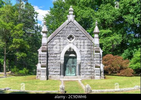 Mausoleo in pietra con simboli cristiani e cancello in ferro battuto con alberi sullo sfondo, al cimitero Sleepy Hollow nell'Upstate NY Foto Stock