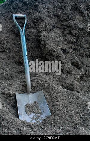 Una grande pala quadrata nera riposante su un pile di pacciamatura di legno nero Foto Stock