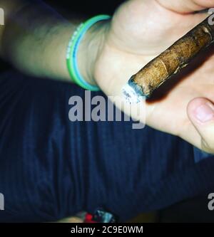 Un uomo caucasico che tiene un Cigar di Cannabis che brucia Foto Stock