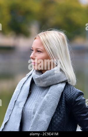 Giovane bella donna bionda che pensa contro la vista offuscata del fiume Foto Stock