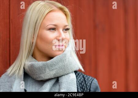 Giovane bella donna bionda che pensa mentre si appoggia contro il muro di legno rosso Foto Stock