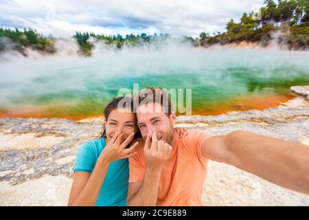 Divertenti coppie selfie turisti a New Zealand Pools viaggiare. I giovani che fanno l'oca faccia all'odore cattivo zolfo odore alle terme geotermiche colorate Foto Stock