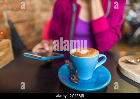 Cafe donna che beve una tazza di caffè cappuccino utilizzando l'app per telefono cellulare. Stile di vita urbano giovani dipendenti dai social media online. Foto Stock