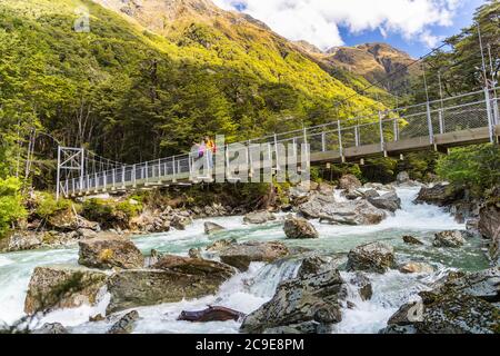 New Zealand escursionisti turisti che attraversano il ponte sul fiume. Coppia tramping zaino in spalla donna, uomo trekking insieme con zaini sul percorso Routeburn Track Foto Stock