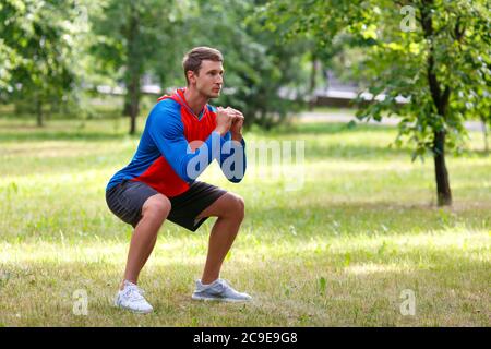 Giovane attraente uomo che squatting all'aperto nel parco. Concetto di uno stile di vita attivo e di uno stile di vita sano. Foto Stock