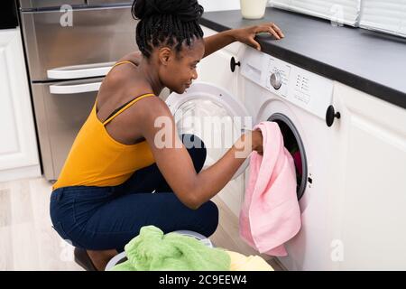 Donna di carico panni sporchi in lavatrice per il lavaggio in una camera di servizio Foto Stock