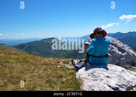 Donna anziana seduta sulla cima della montagna con bella vista sullo sfondo - Velebit montagna, Croazia Foto Stock