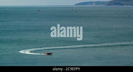 Vista aerea di una barca a velocità rossa a vela veloce con qualcuno sci d'acqua sul retro a Poole Bay, Regno Unito ci sono numerose navi nella baia con panoramico Foto Stock