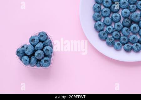 Mirtilli in una ciotola a forma di cuore, bacche su un piatto rosa, piatto. Sfondi astratti, sfondo estivo luminoso. Messa a fuoco selettiva Foto Stock