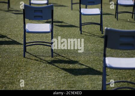 Sedie l'una dall'altra per mantenere la distanza sociale durante l'epidemia di Covid-19 in un evento all'aperto sul tappeto erboso di uno stadio. Foto Stock