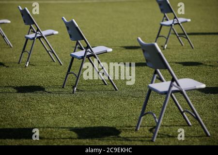 Sedie l'una dall'altra per mantenere la distanza sociale durante l'epidemia di Covid-19 in un evento all'aperto sul tappeto erboso di uno stadio. Foto Stock