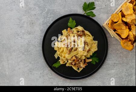 Tagliatelle di pasta italiana con funghi chanterelle e prezzemolo in un piatto nero Foto Stock
