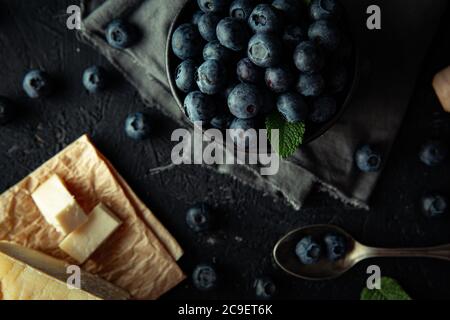 Gruppo di mirtilli biologici con foglie di menta fresca, accanto al formaggio fatto in casa, su sfondo scuro. Foto Stock