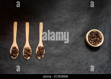 vista dall'alto dei cucchiai e della ciotola in legno riempiti di chicchi di caffè arrosto su sfondo di ardesia scuro. formato orizzontale con spazio per la copia del testo Foto Stock