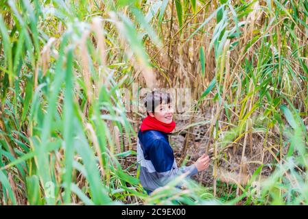 Ragazzo sorridente che si nasconde dietro un cespuglio nel bosco Foto Stock