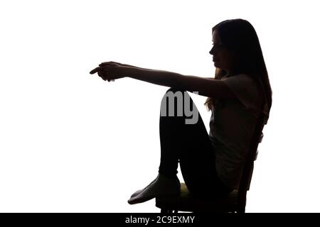 Giovane bella ragazza in meditazione si siede su una sedia e ha abbassato le mani - silhouette Foto Stock