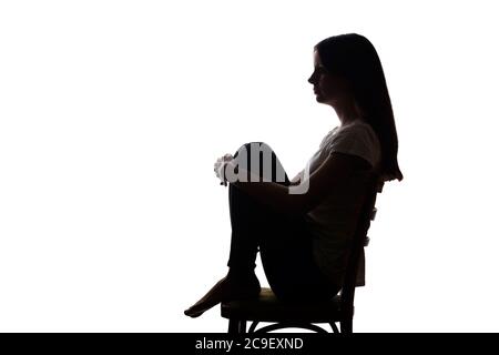 Giovane bella ragazza in dolore abbracciò le ginocchia e le lasciò cadere le mani - silhouette Foto Stock