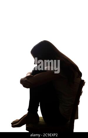 Giovane bella ragazza in dolore abbracciò le ginocchia e le lasciò cadere le mani - silhouette Foto Stock